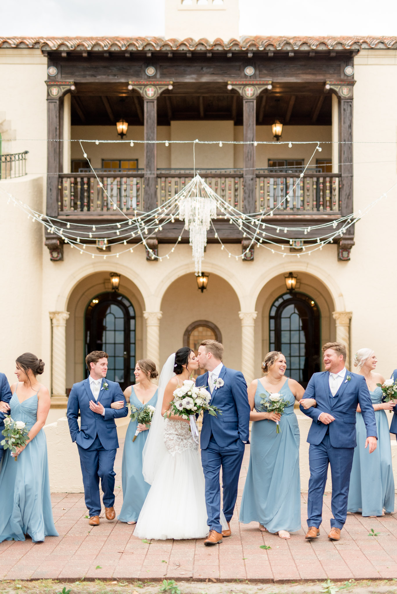 Bride and groom kiss while walking with wedding party.