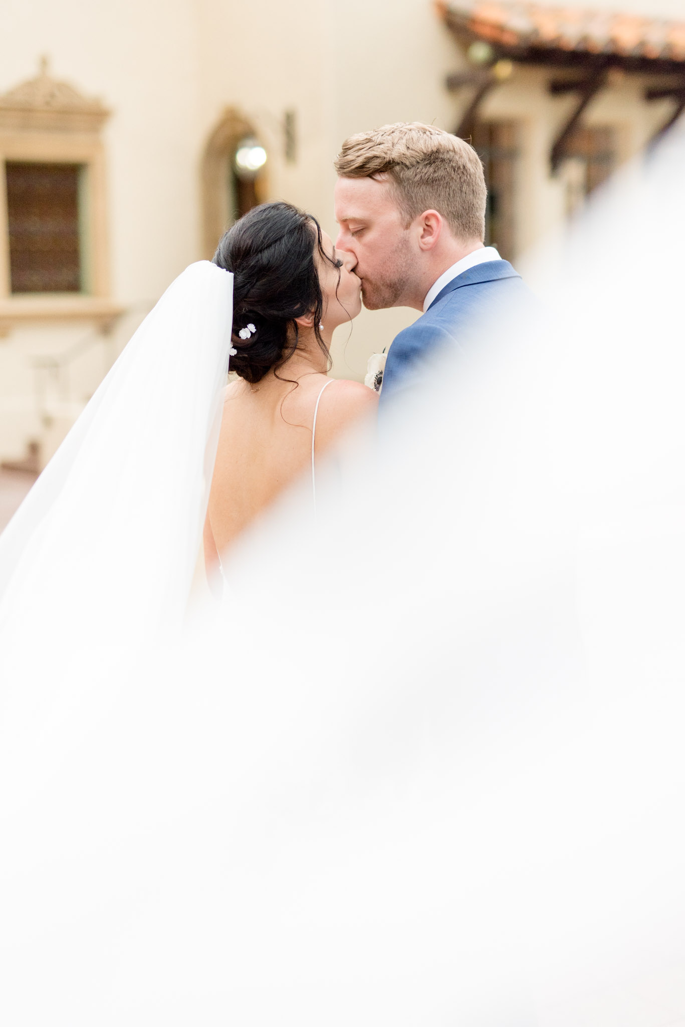 Bride and groom kiss behind veil.