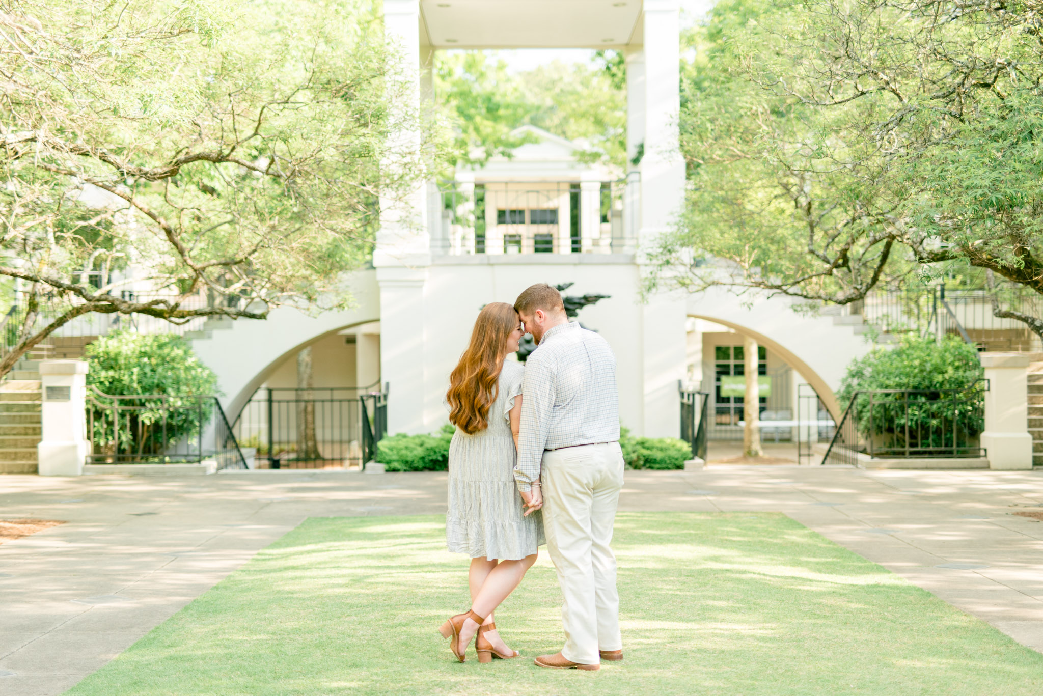 Couple snuggles in front of white building.