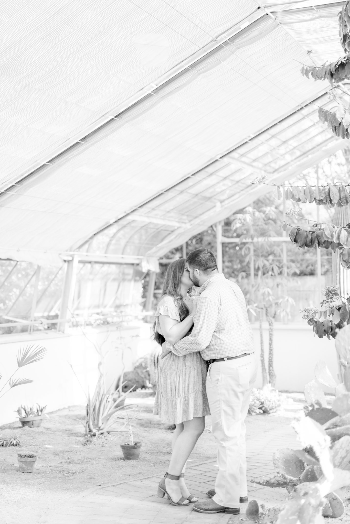 Couple kisses in greenhouse.