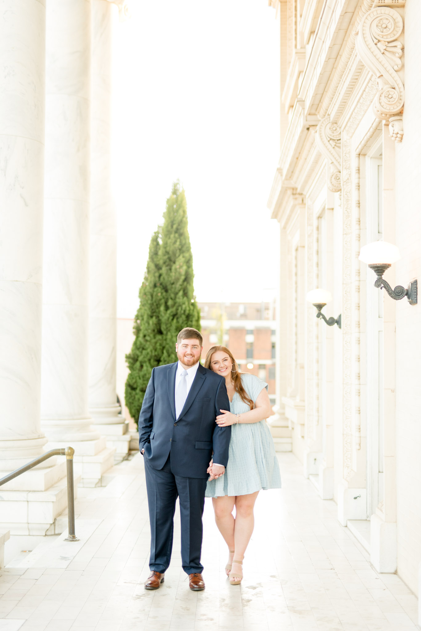 Couple smiles at camera in marble hallway.