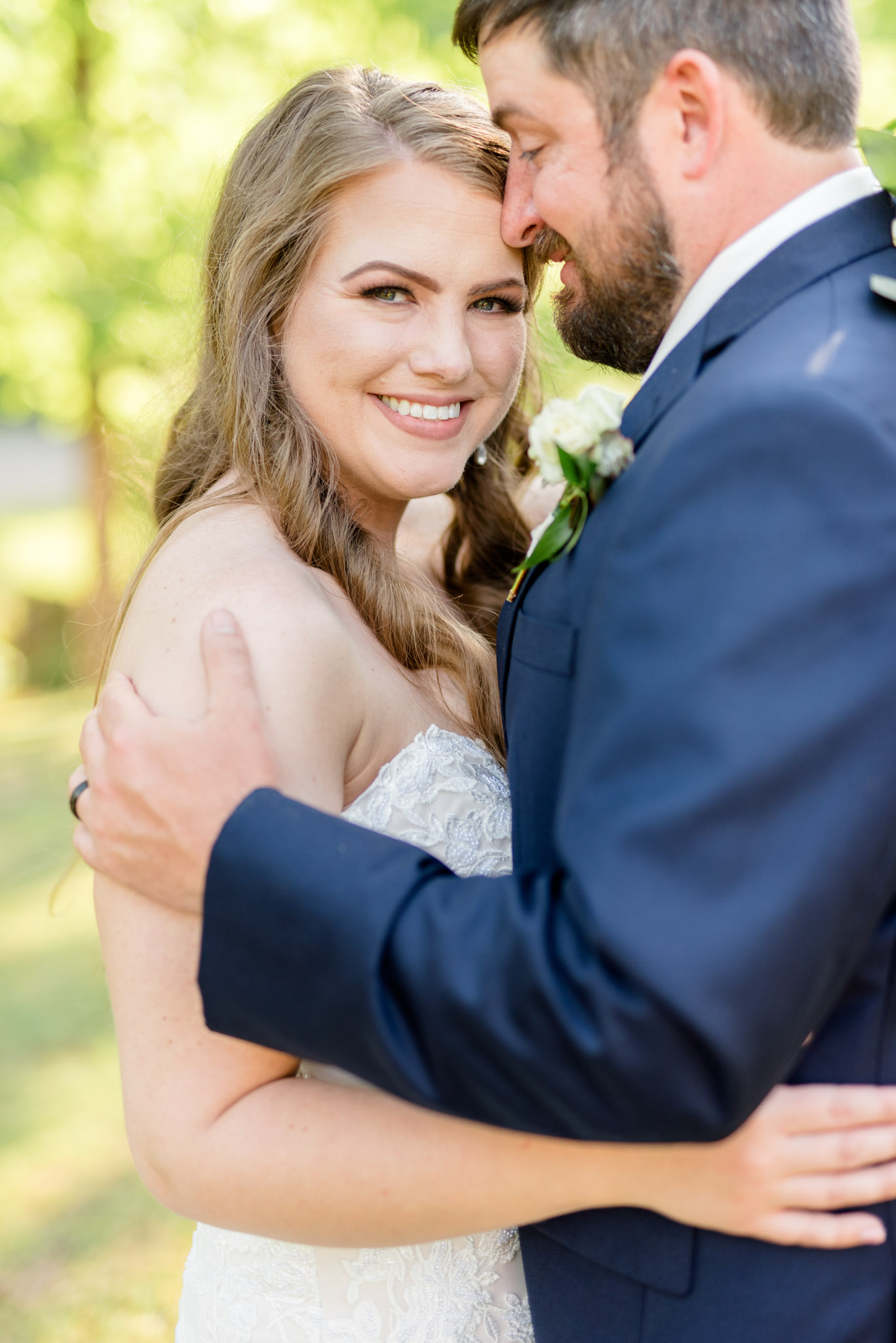 Bride smiles at camera while groom snuggles.