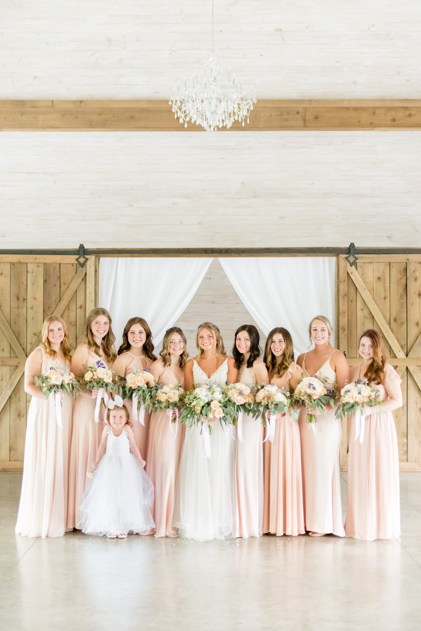 Bride and bridesmaids smile at camera under chandelier.