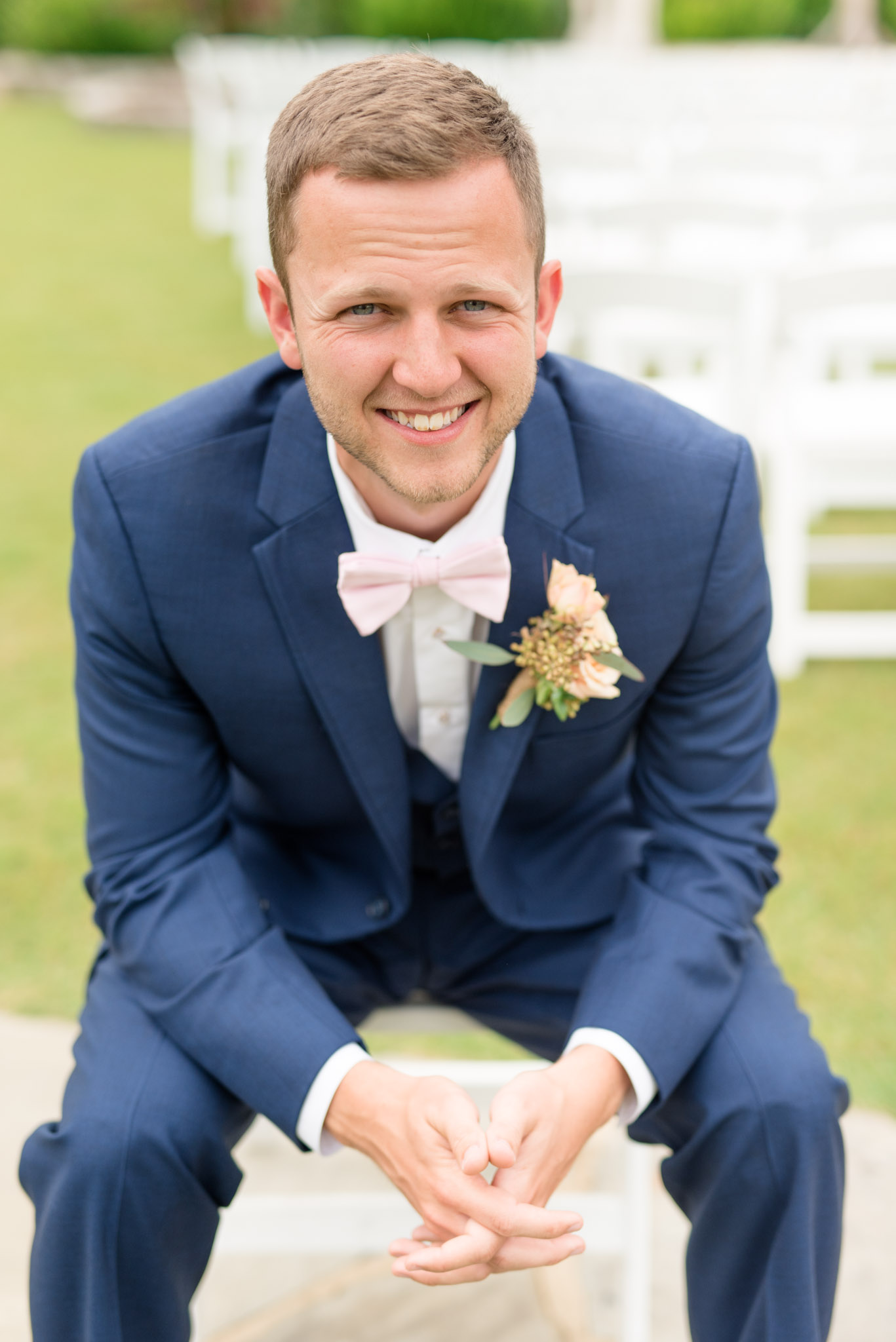 Groom smiles while sits on chair.