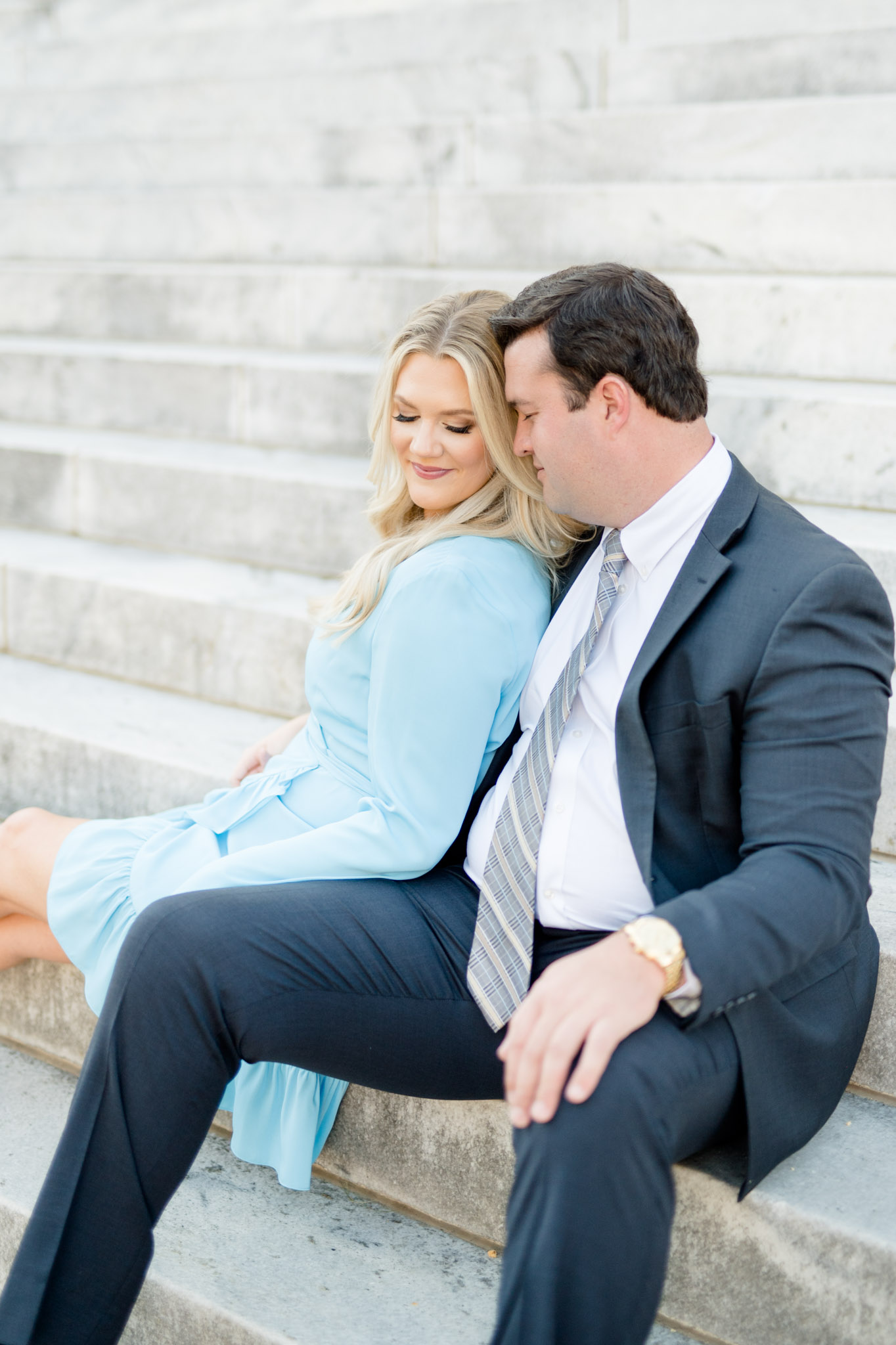 Couple snuggles on marble staircase.