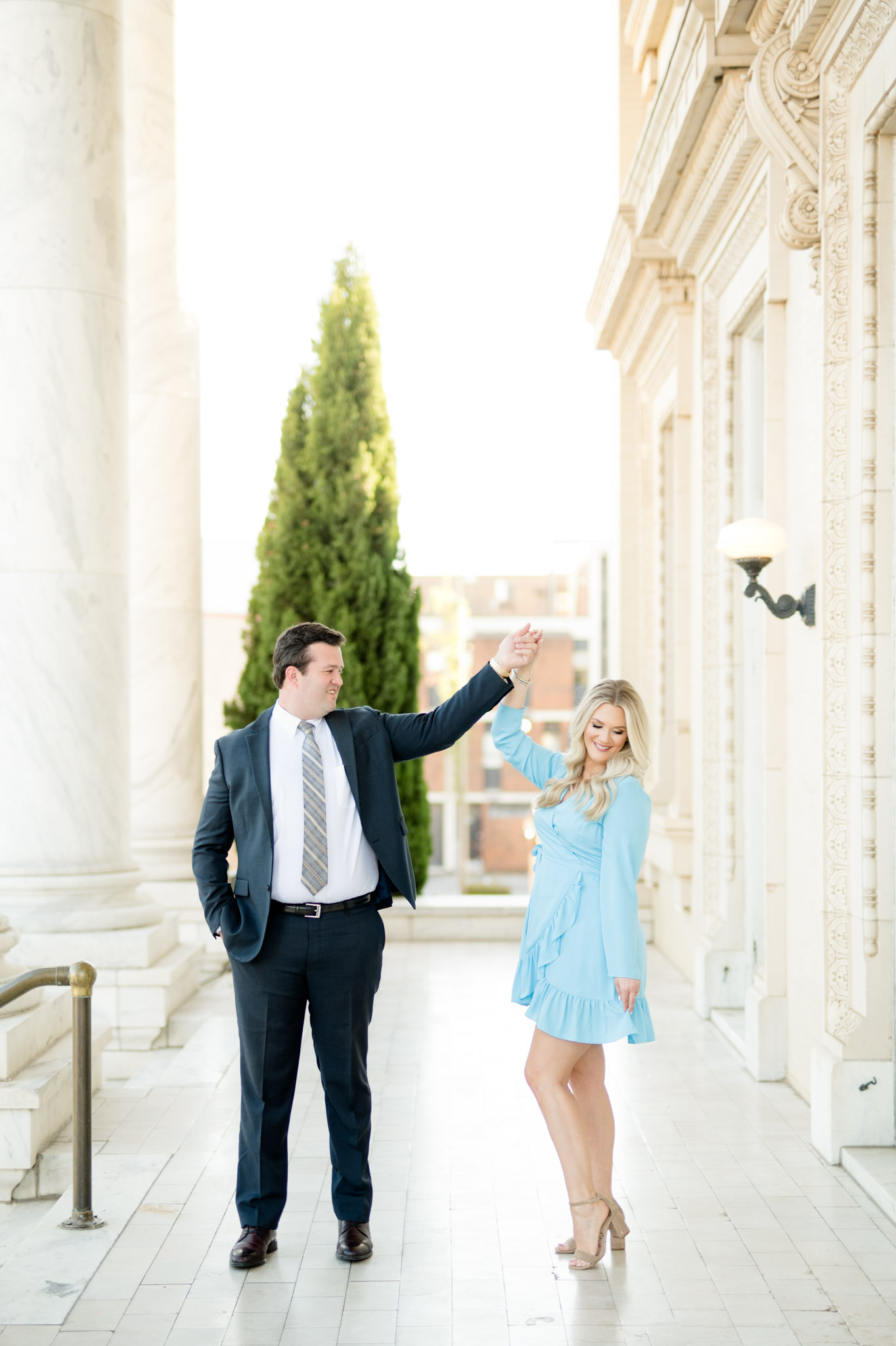 Man twirls fiance in marble hallway.