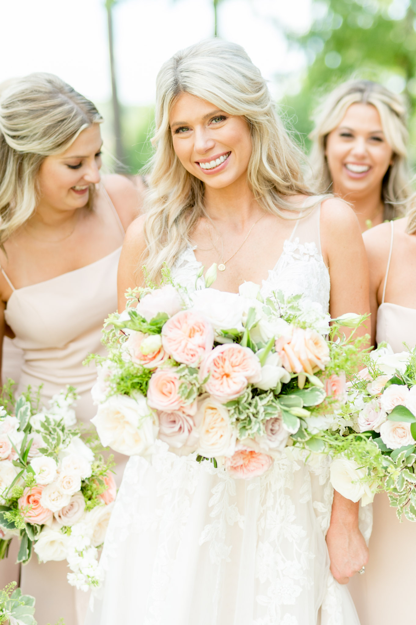 Bride smiles at camera while bridesmaids laugh around her.