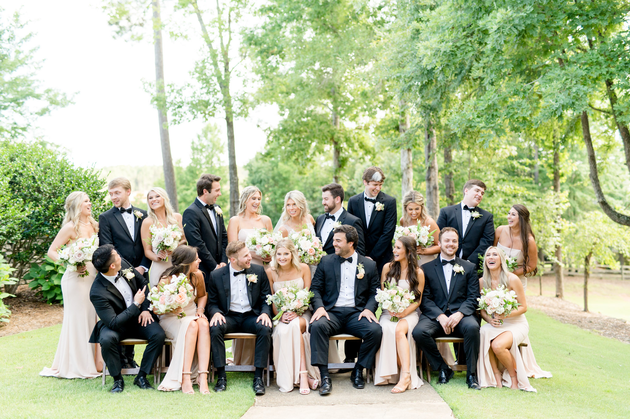 Wedding party surrounds bride and groom and laugh.