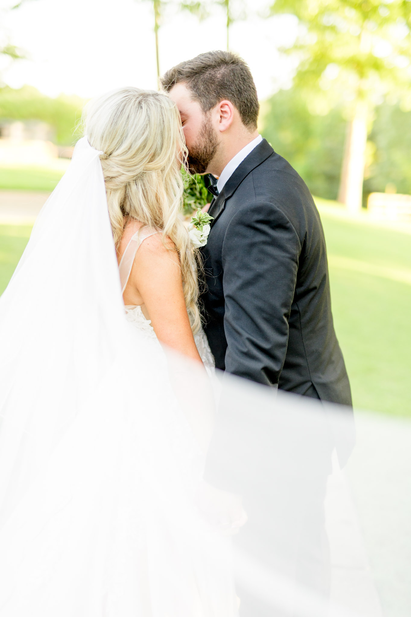 Bride and groom kiss as veil blows.