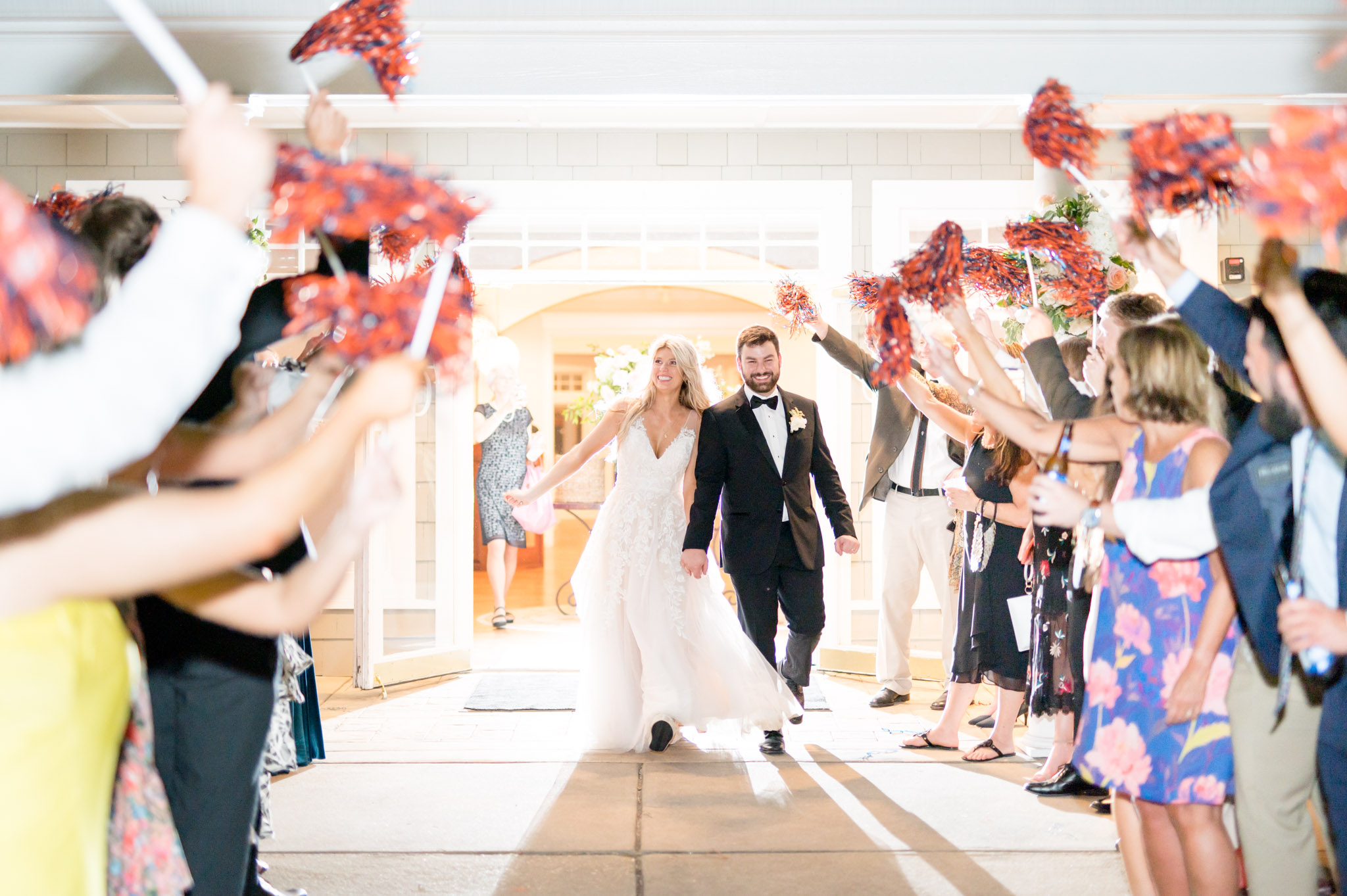 Bride and groom leave reception with guests cheering.