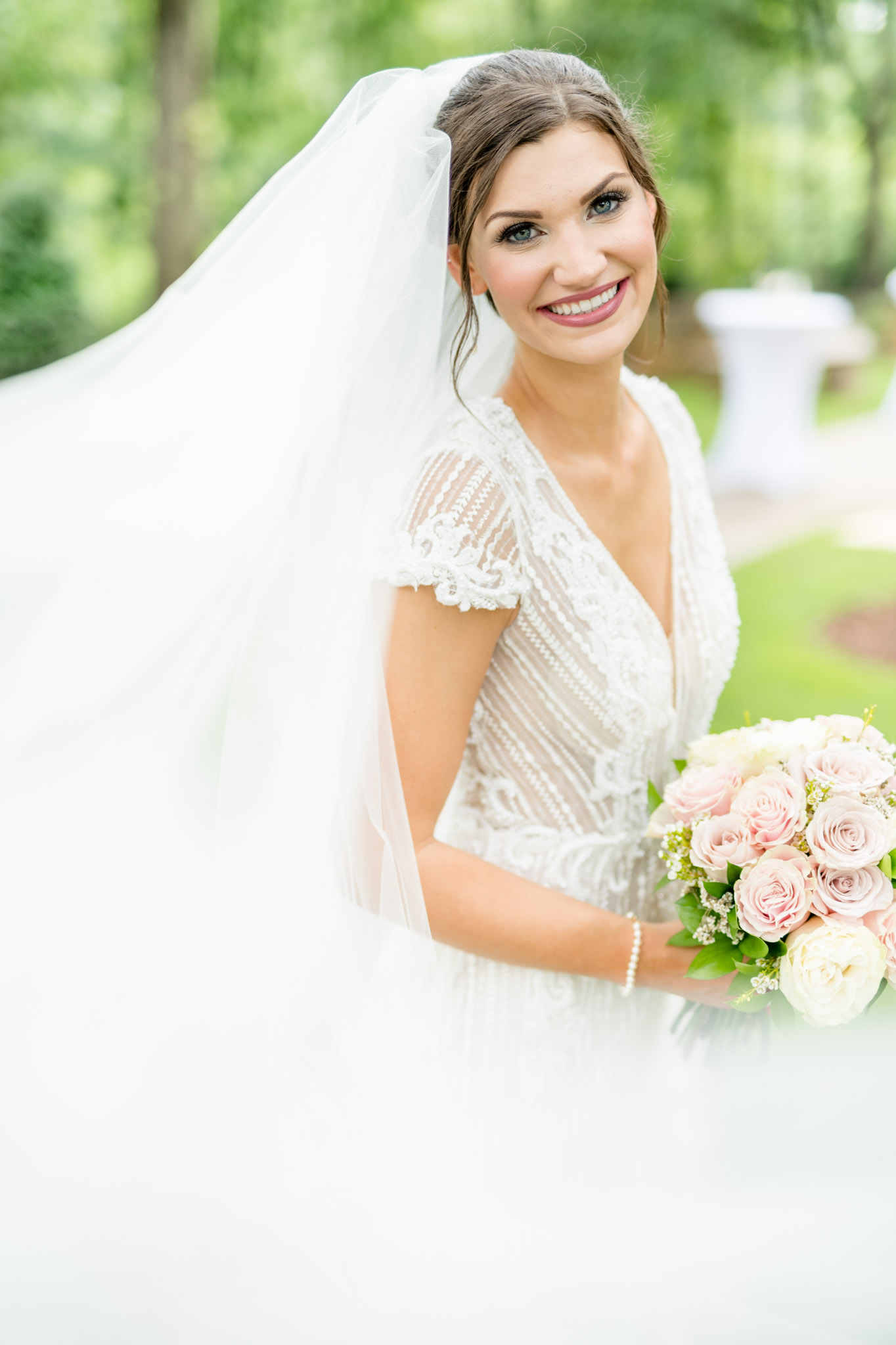 Bride smiles at camera while veil blows in wind.