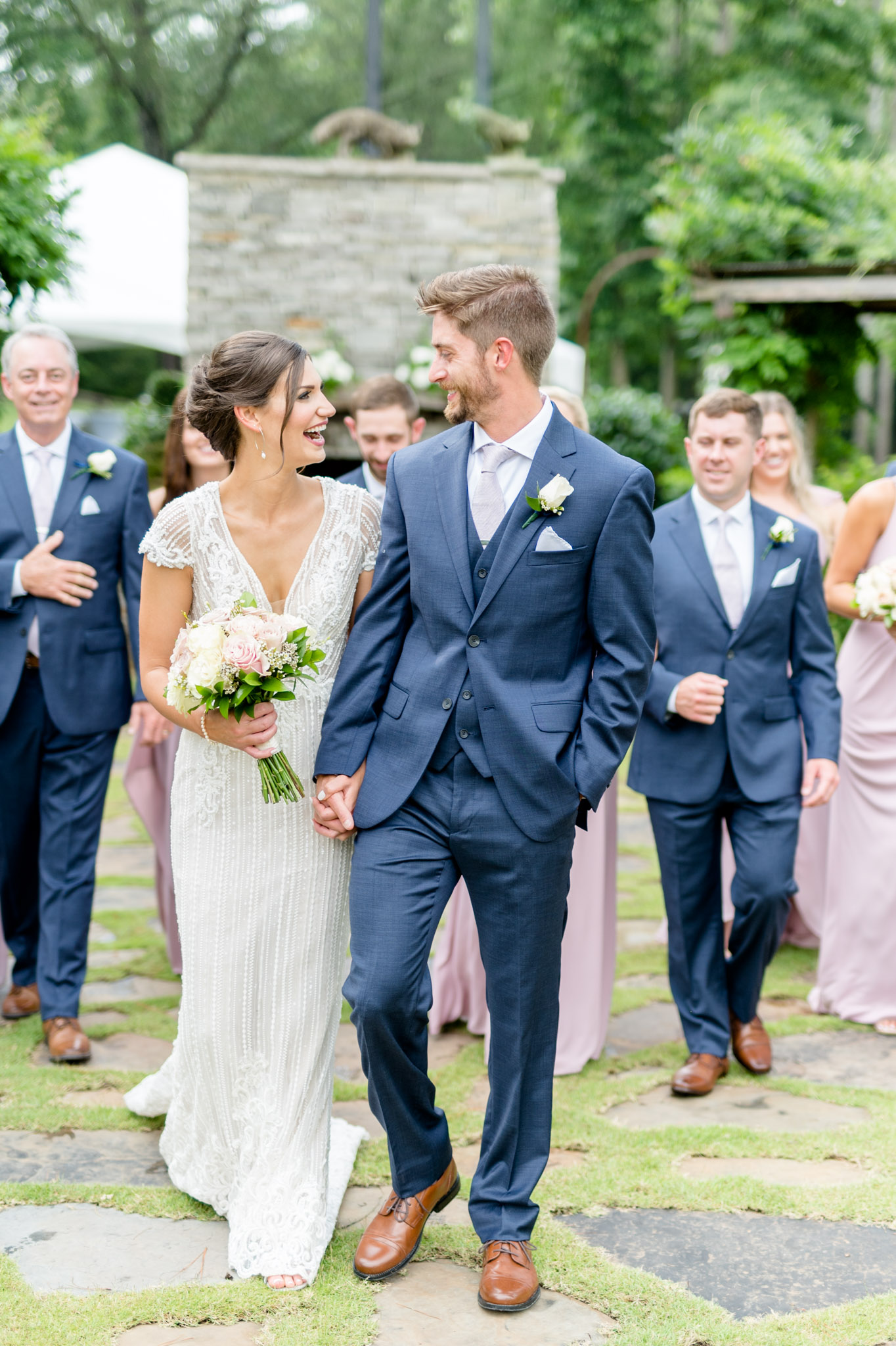 Bride and groom laugh together while walking with wedding party