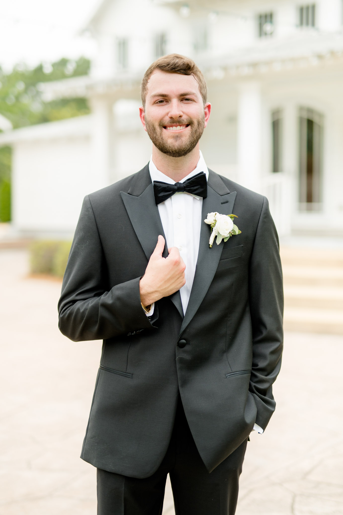 Groom holds lapel and smiles at camera.
