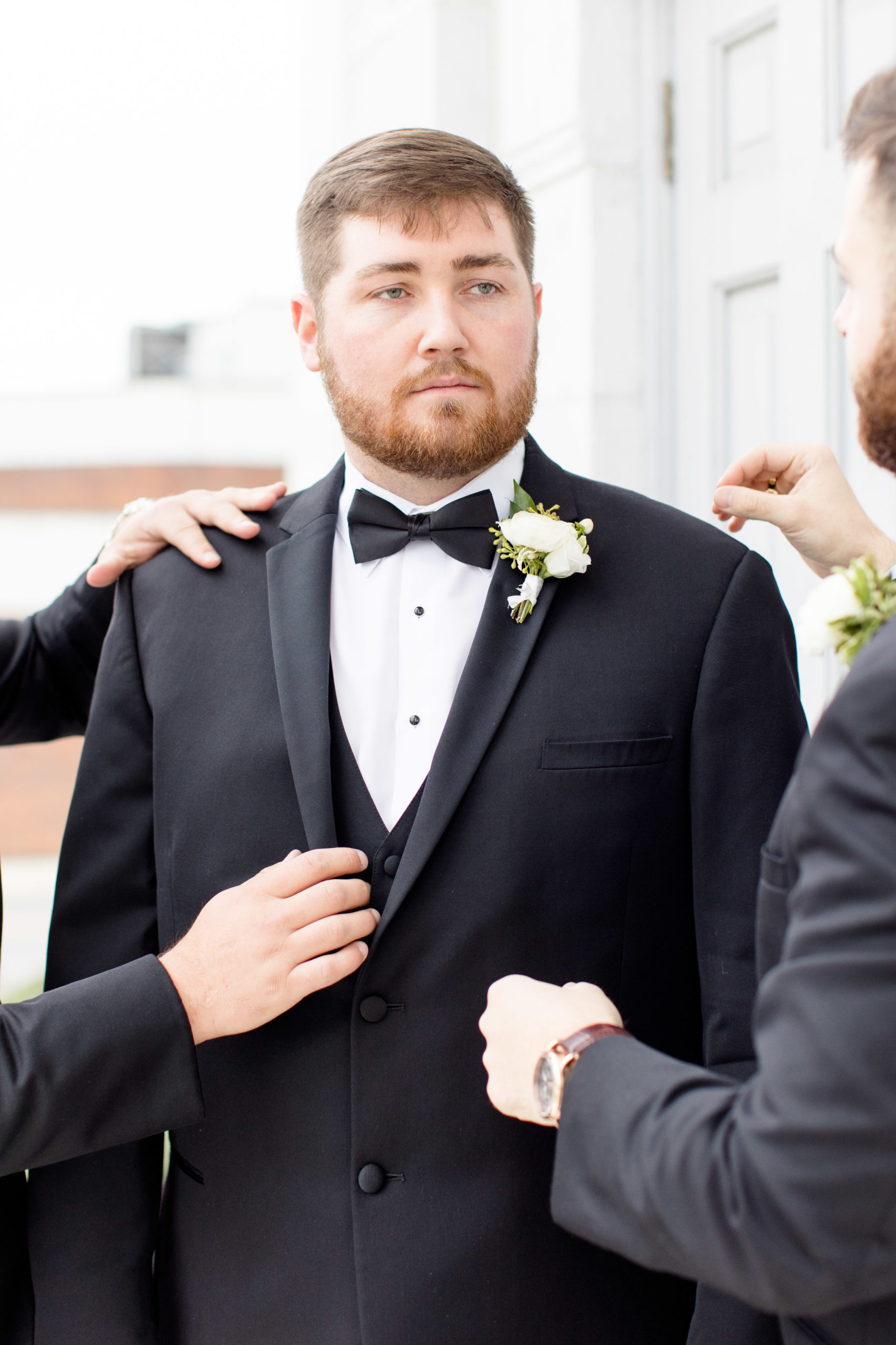 Groomsmen help straighten groom's jacket.