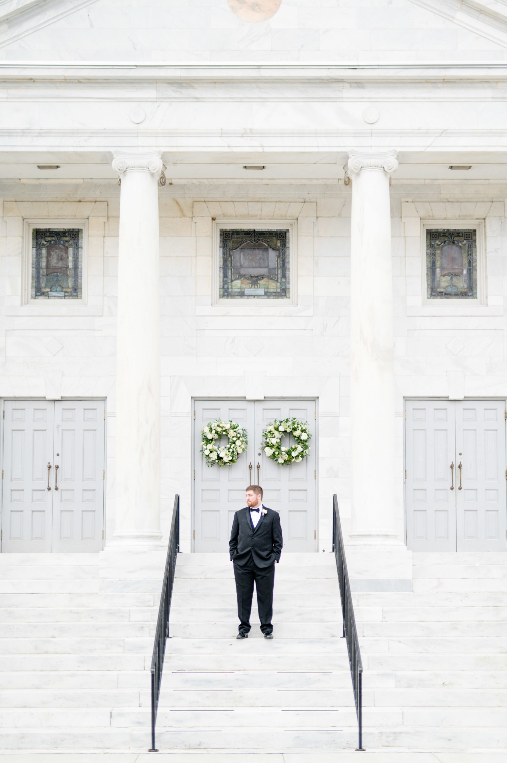 Groom stands on marble steps and looks over shoulder.