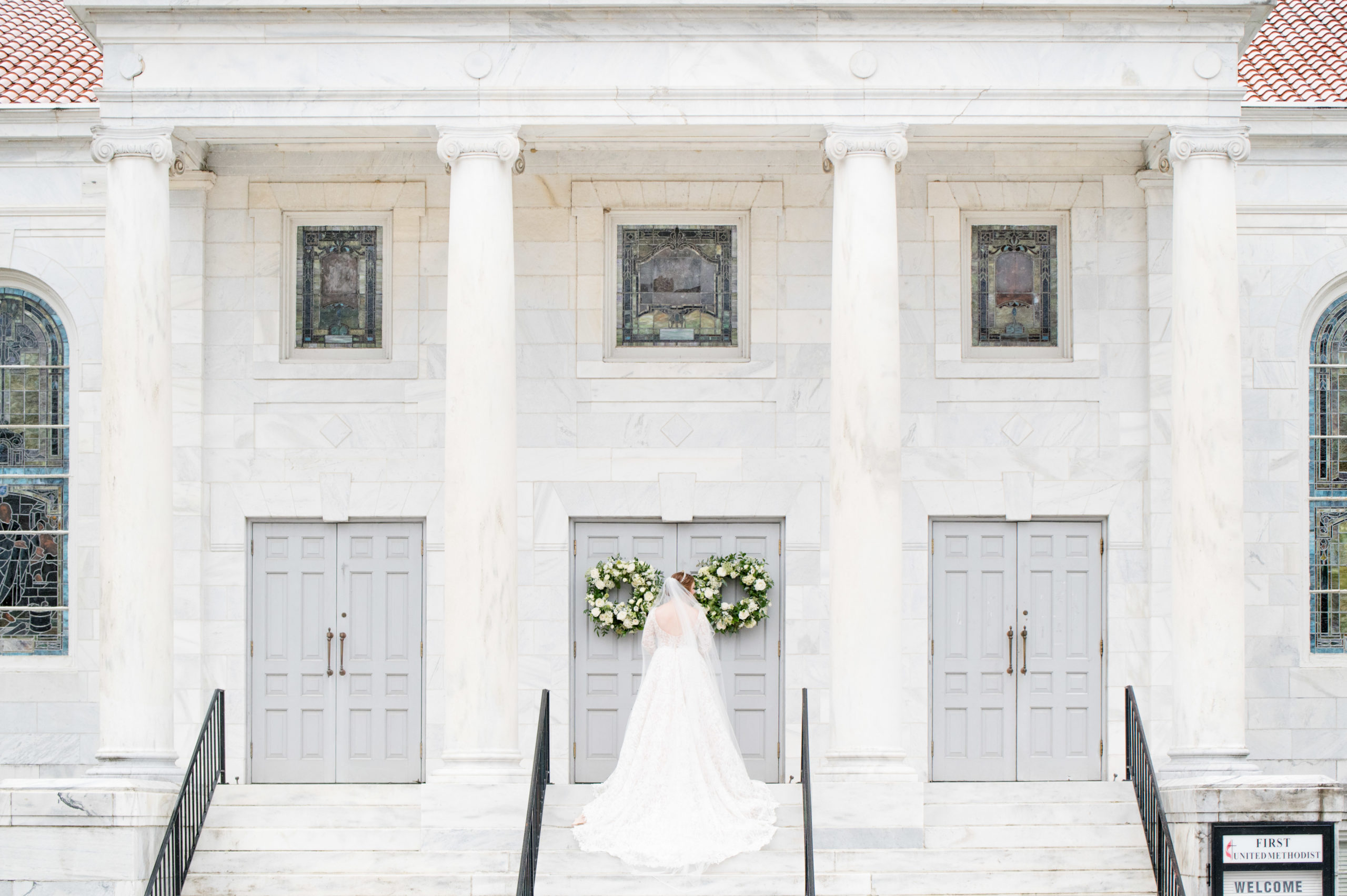 Bride shows off back of dress on marble staircase.