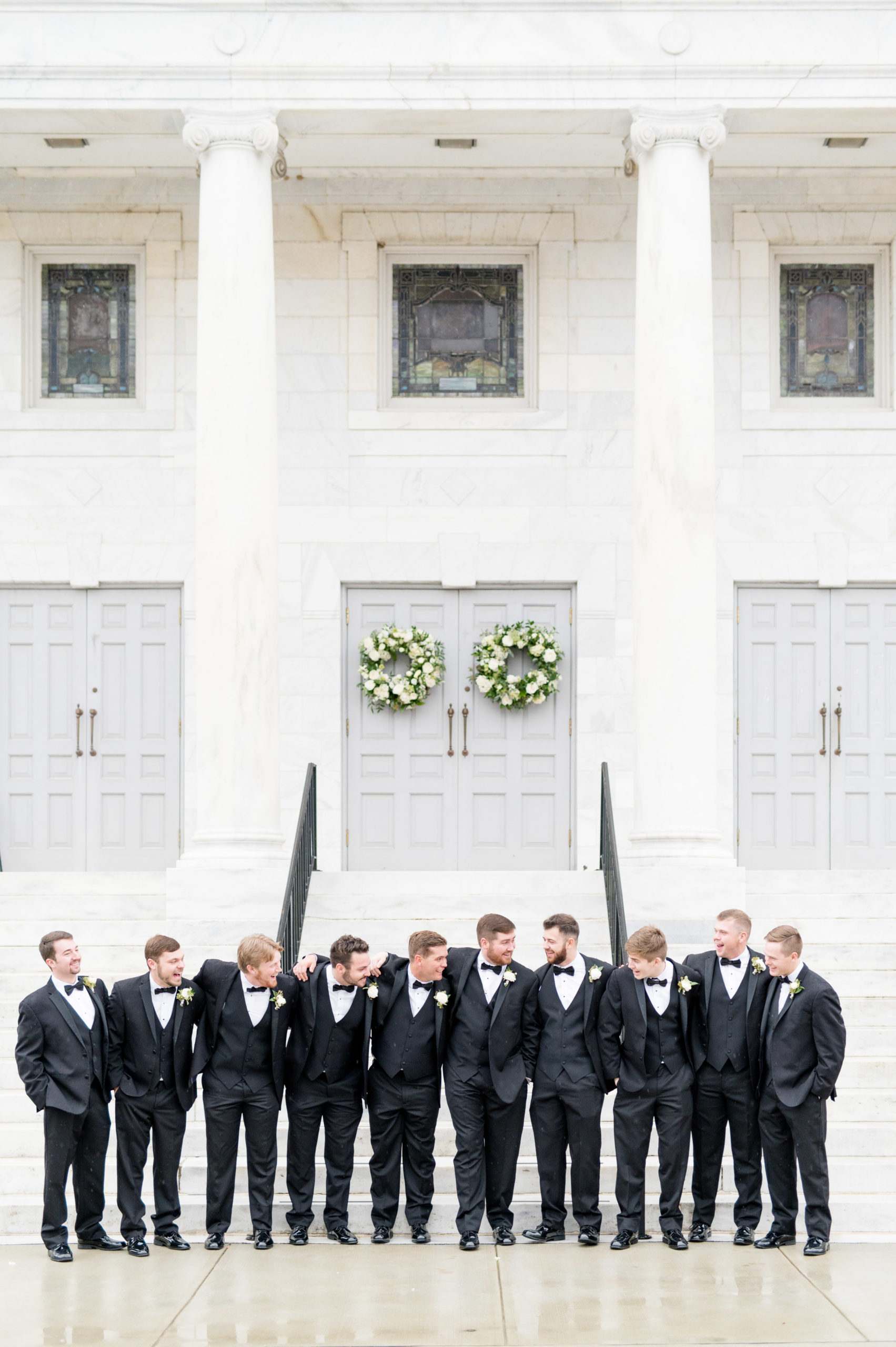 Groom and groomsmen laugh together at white church.
