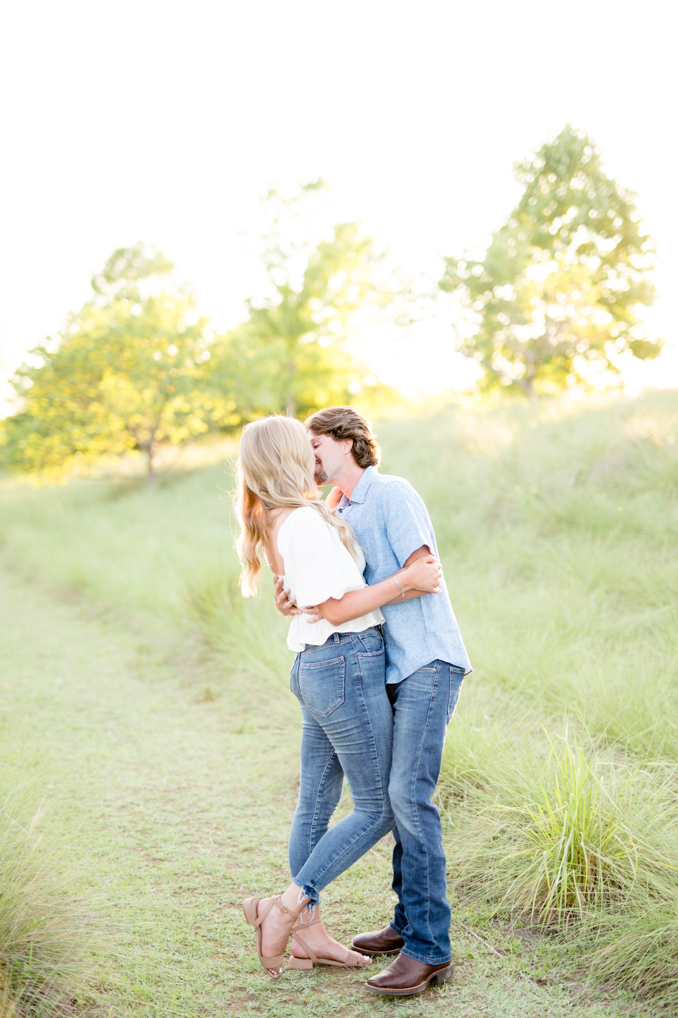 Engaged couple kiss in field at sunset.