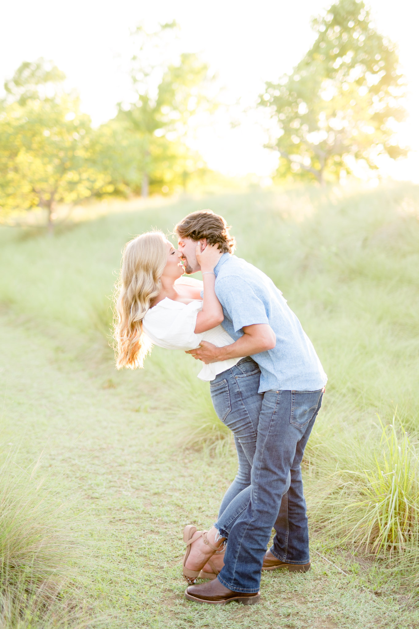 Engaged couple lean back and go in for kiss during sunset.