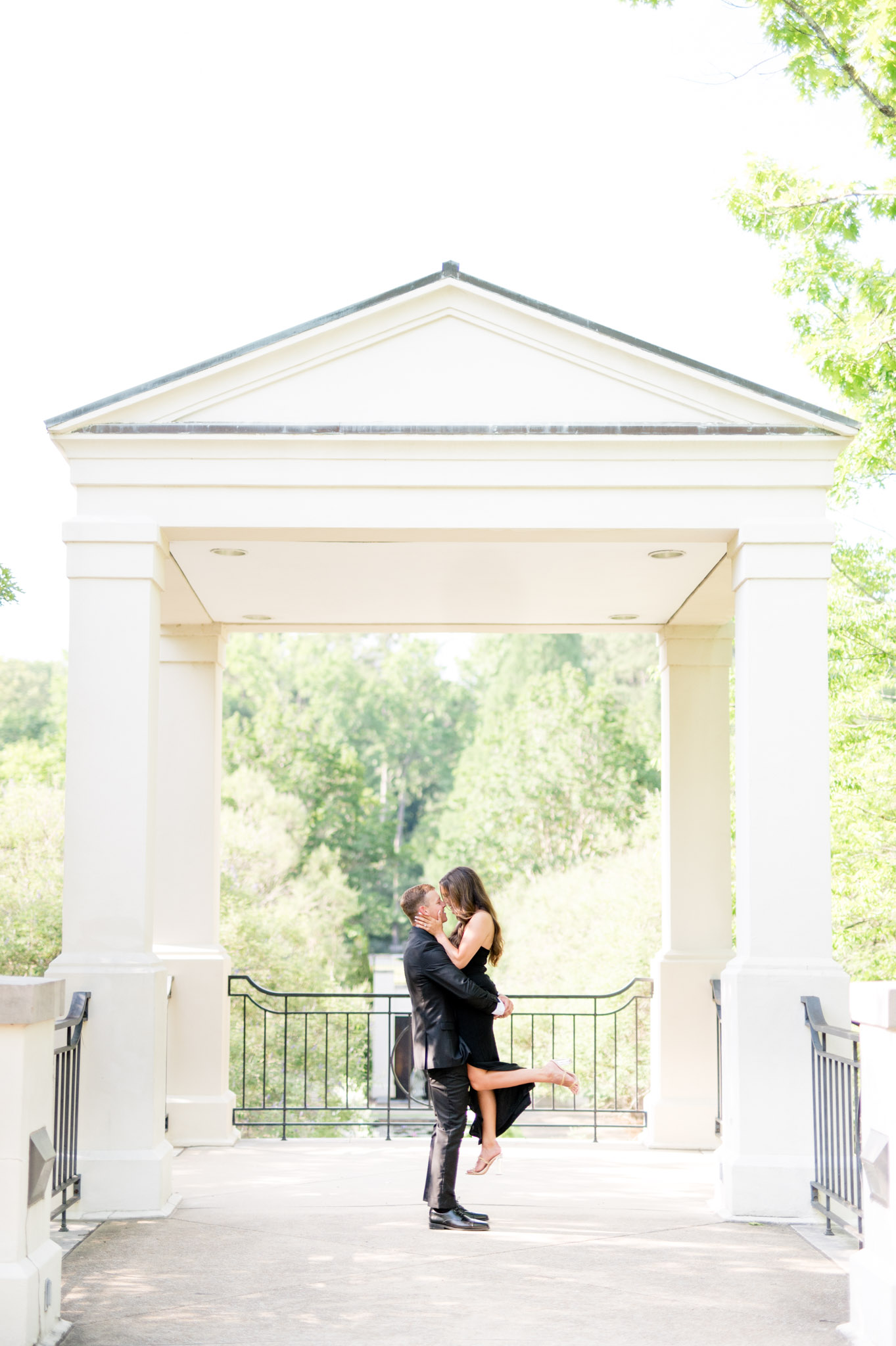 Groom lifts fiance up in front of white pavilion.
