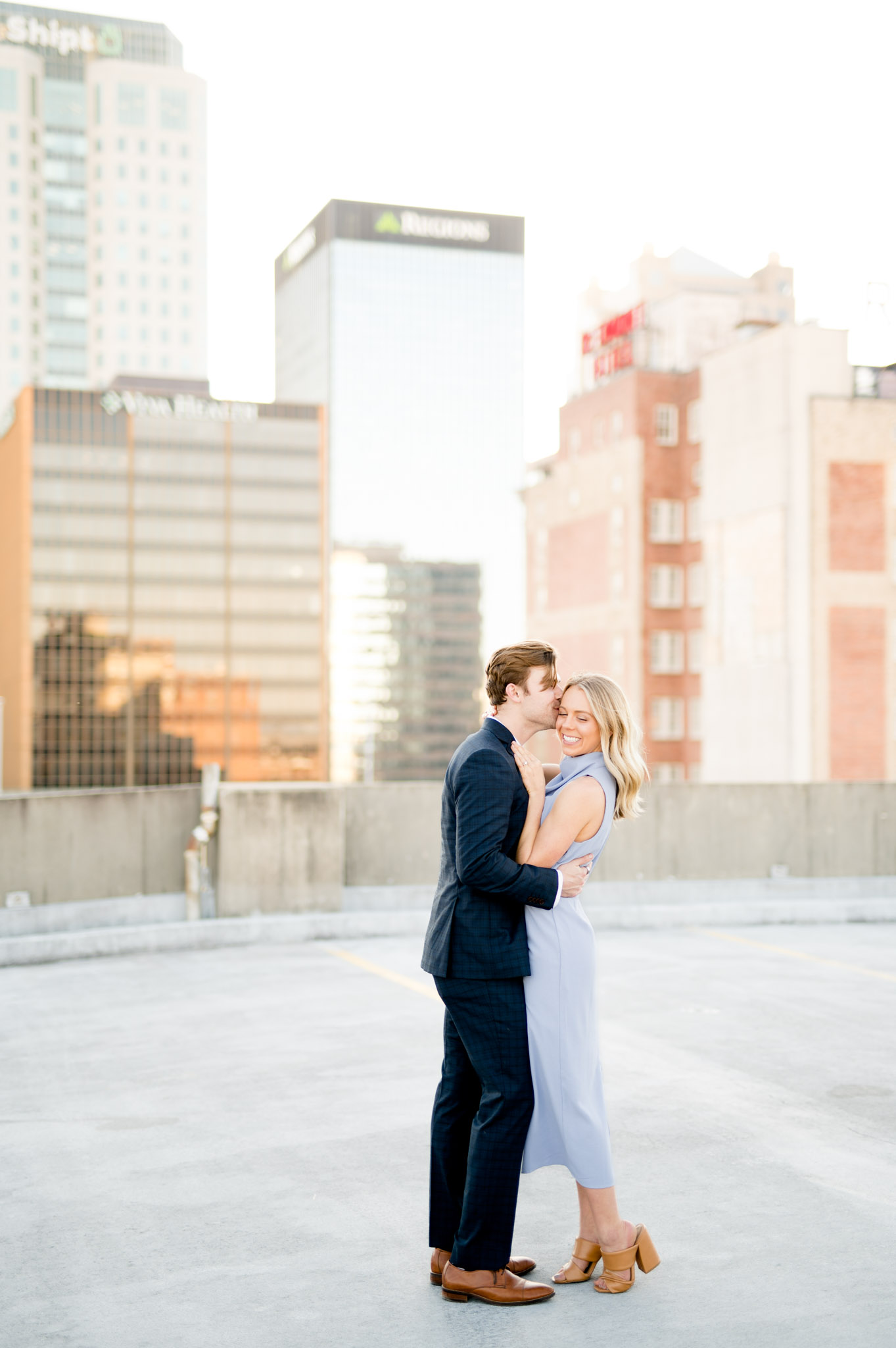 Couple snuggle on city rooftop.