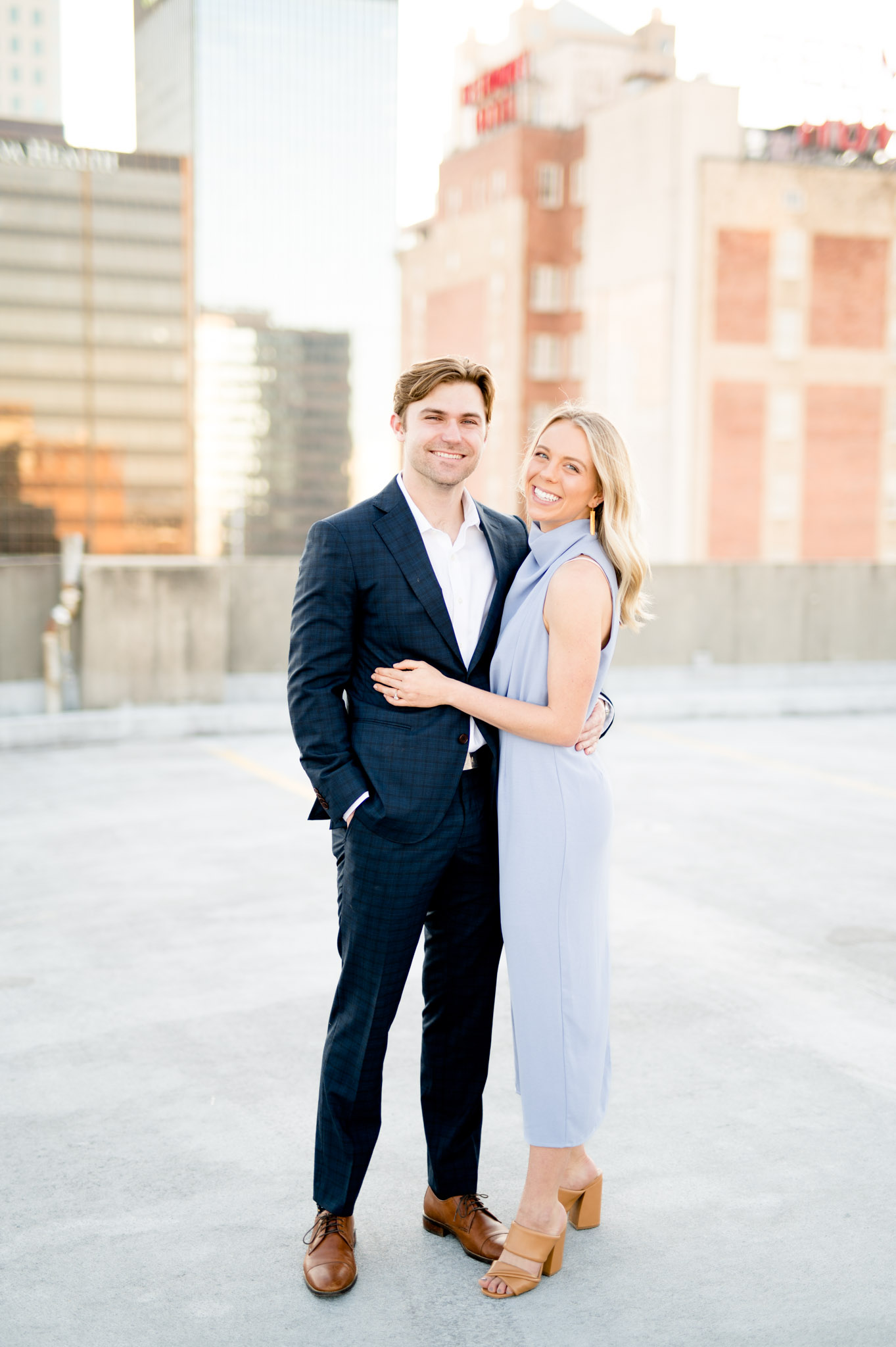 Couple smiles at camera while on city rooftop.