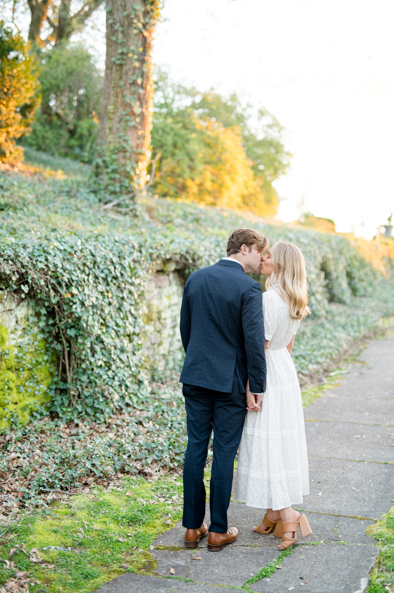 Couple kisses on ivy-covered sidewalk.