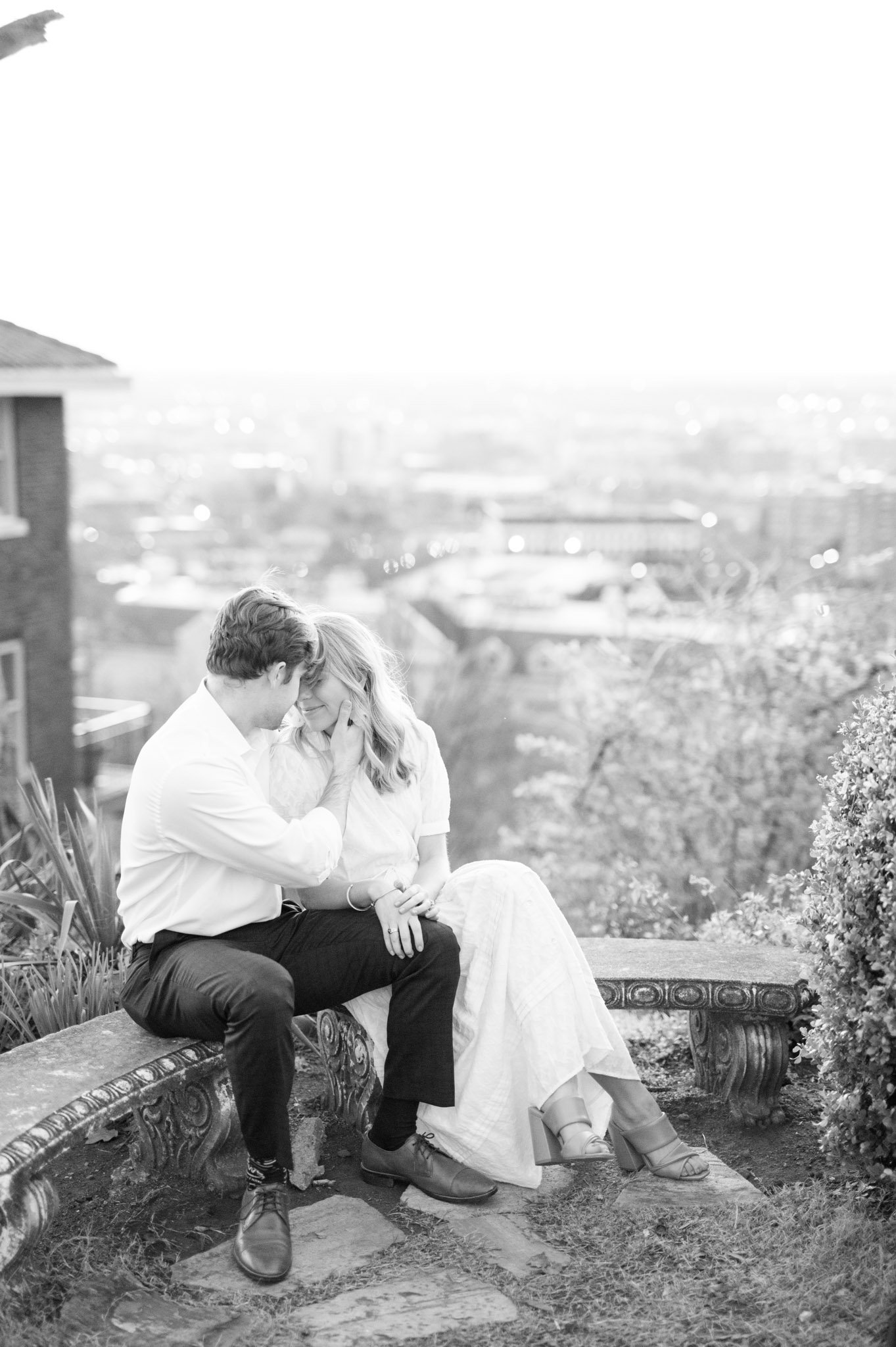Couple cuddle on bench overlooking city.