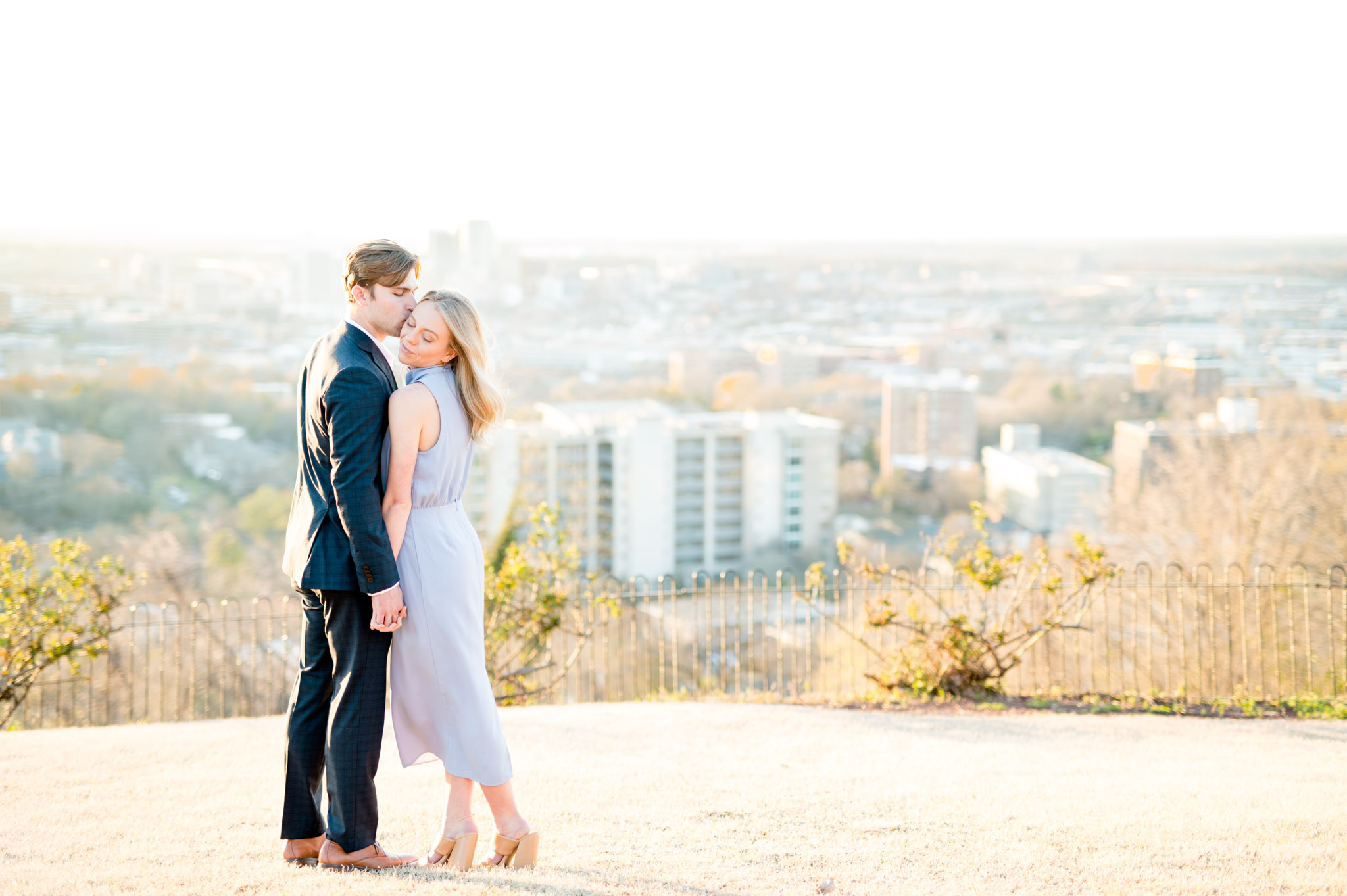 Groom kisses fiance at city overlook.