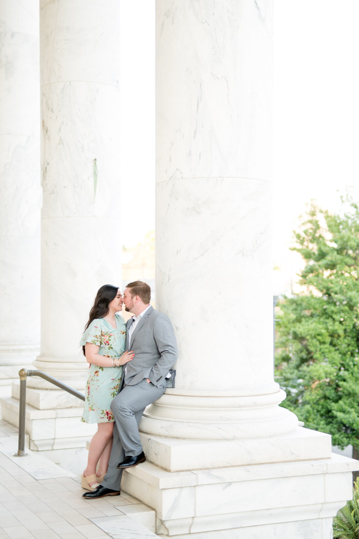 Engaged couple leans against pillar.