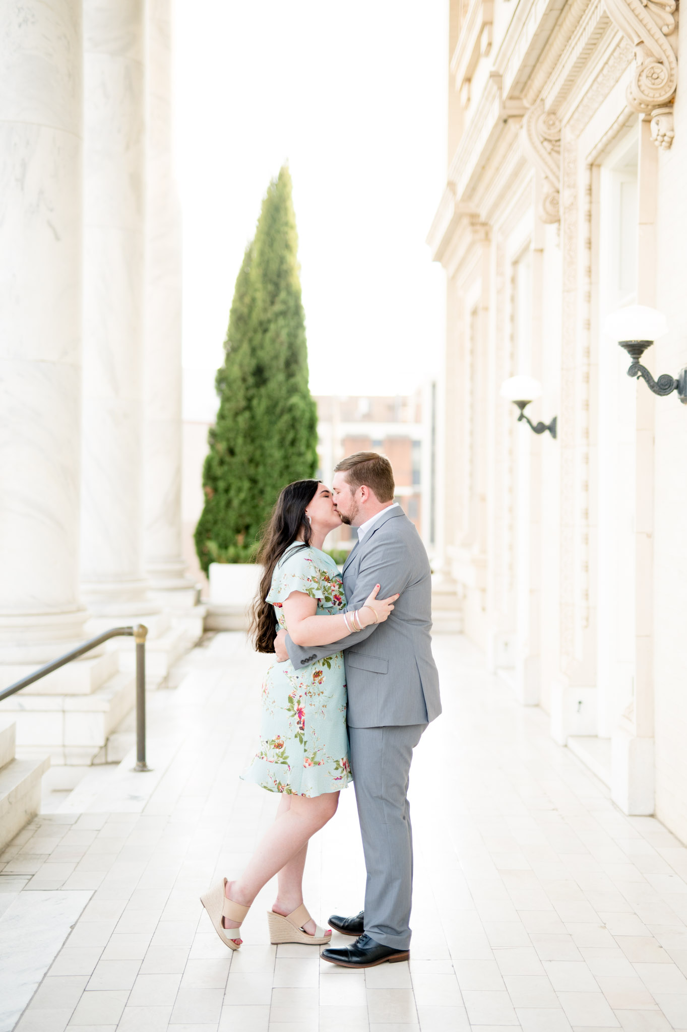 Engaged couple kiss in marble atrium.