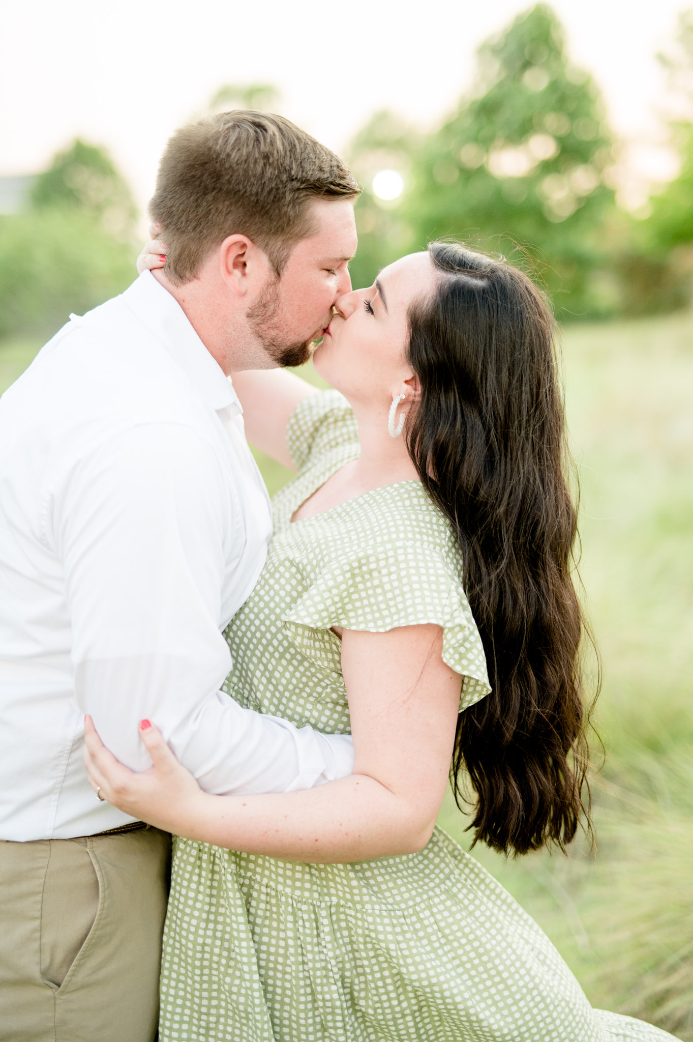 Couple kisses in grassy field.