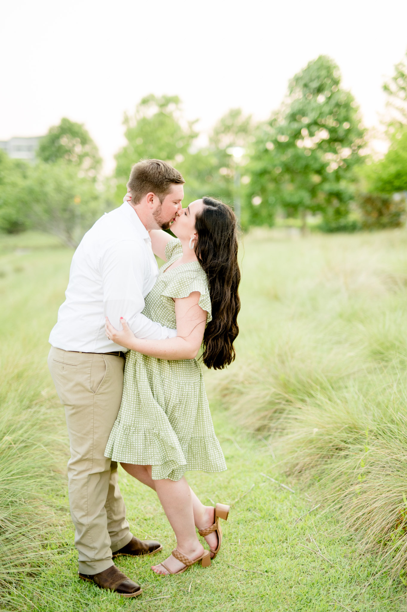 Couple kisses in grassy field.