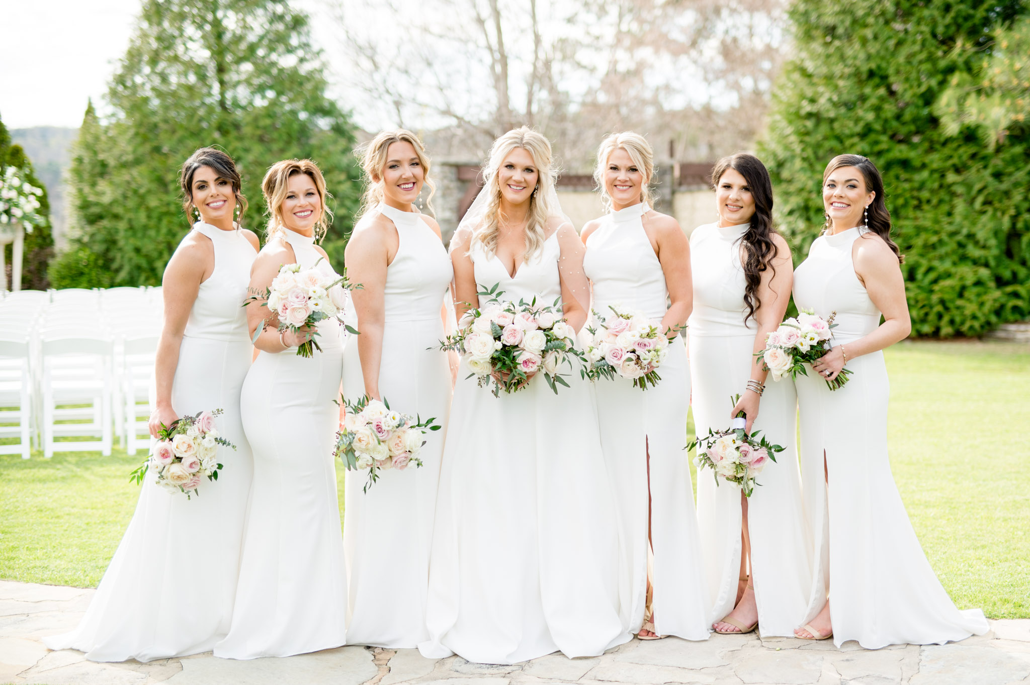 Bride and bridesmaids hold bouquets and smile.