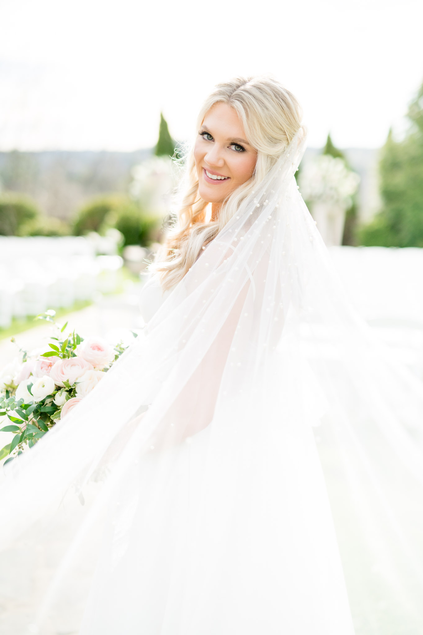 Bride looks at camera while veil blows.