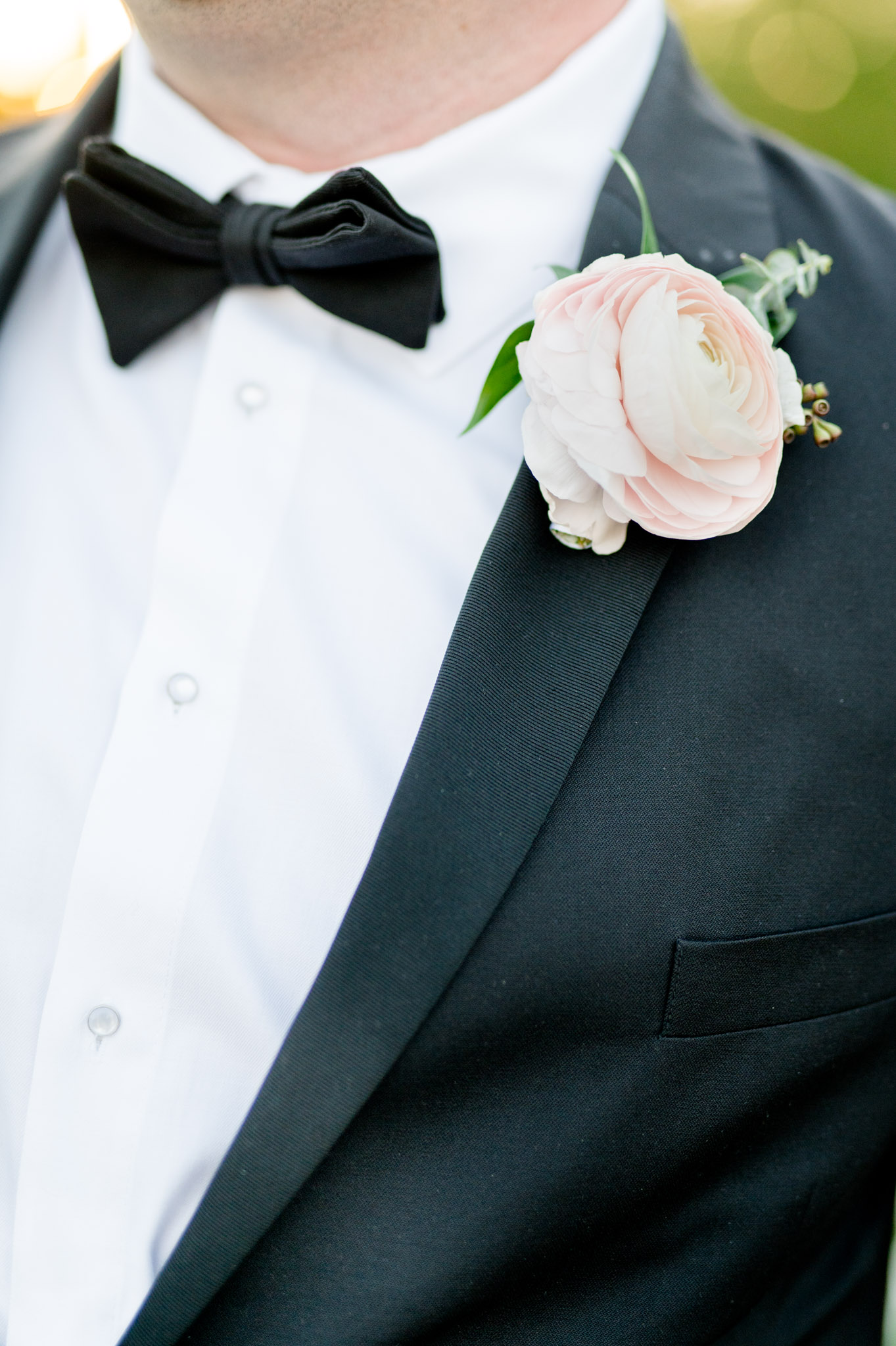 Pink flower boutonniere pinned on groom's lapel.