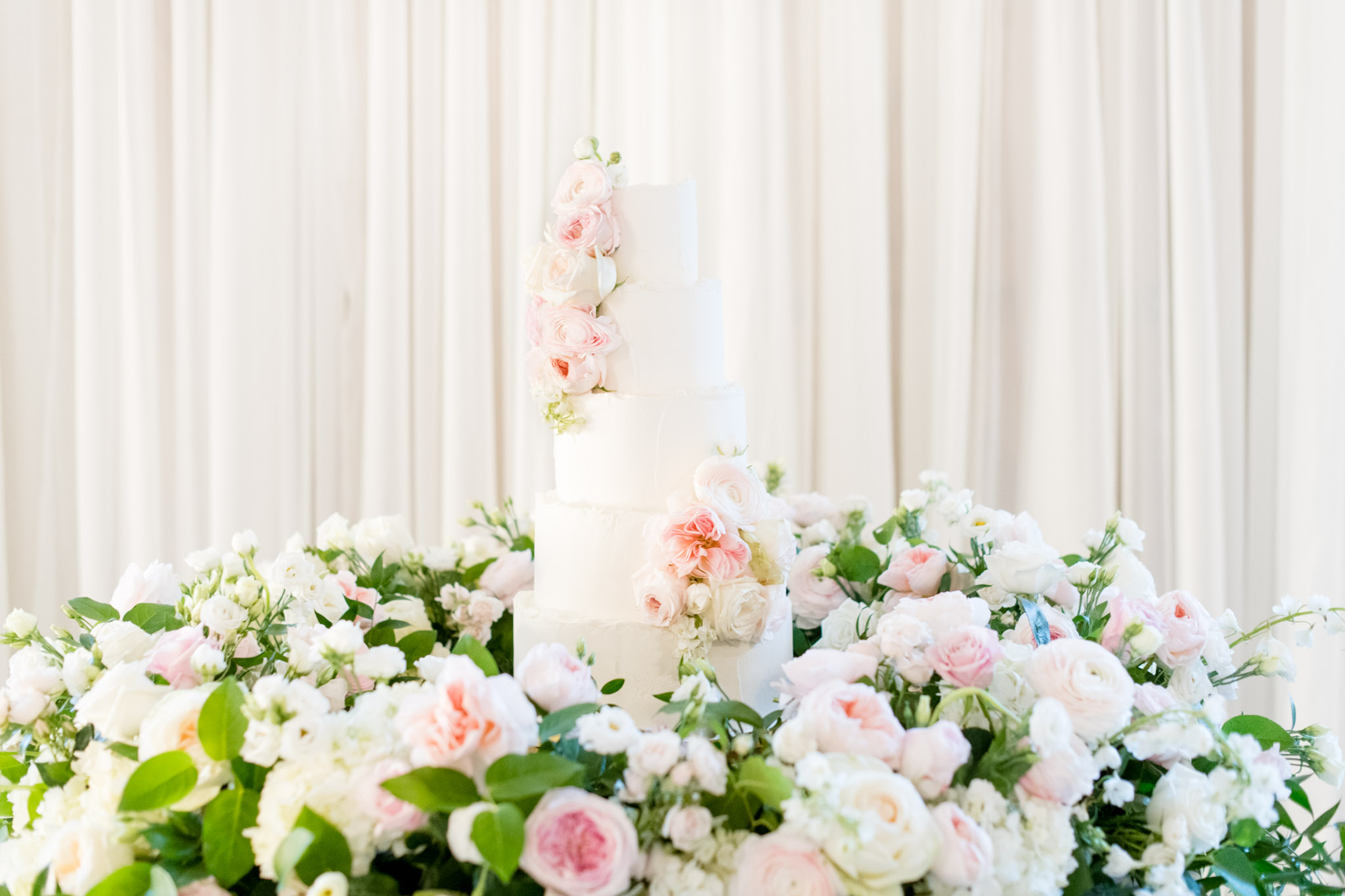 White cake with pink flowers sits on table at reception.