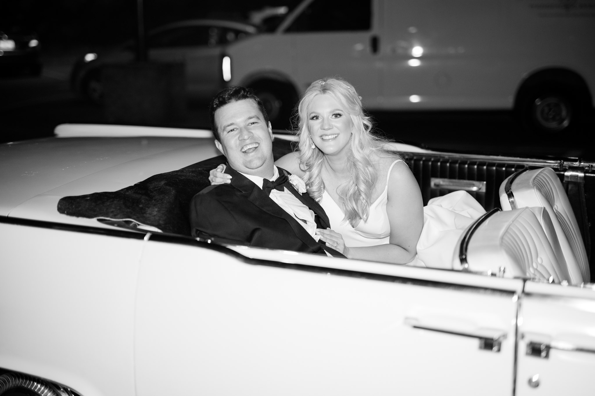 Bride and groom smile from getaway car.
