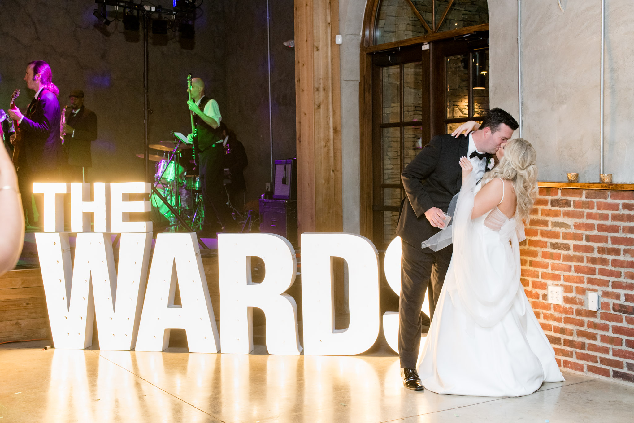Bride and groom kiss next to light up marque letters.